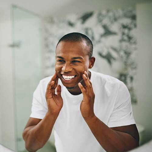 A man smiling and touching his cheeks while looking in the mirror.